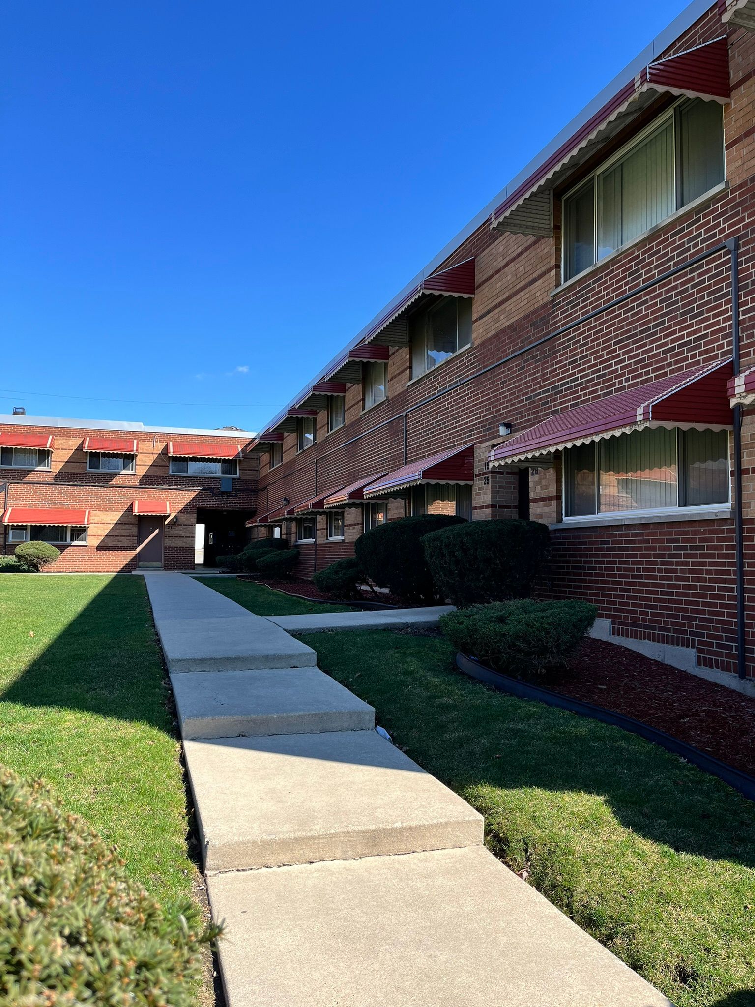 a walkway leading to a brick apartment building with red awnings .
