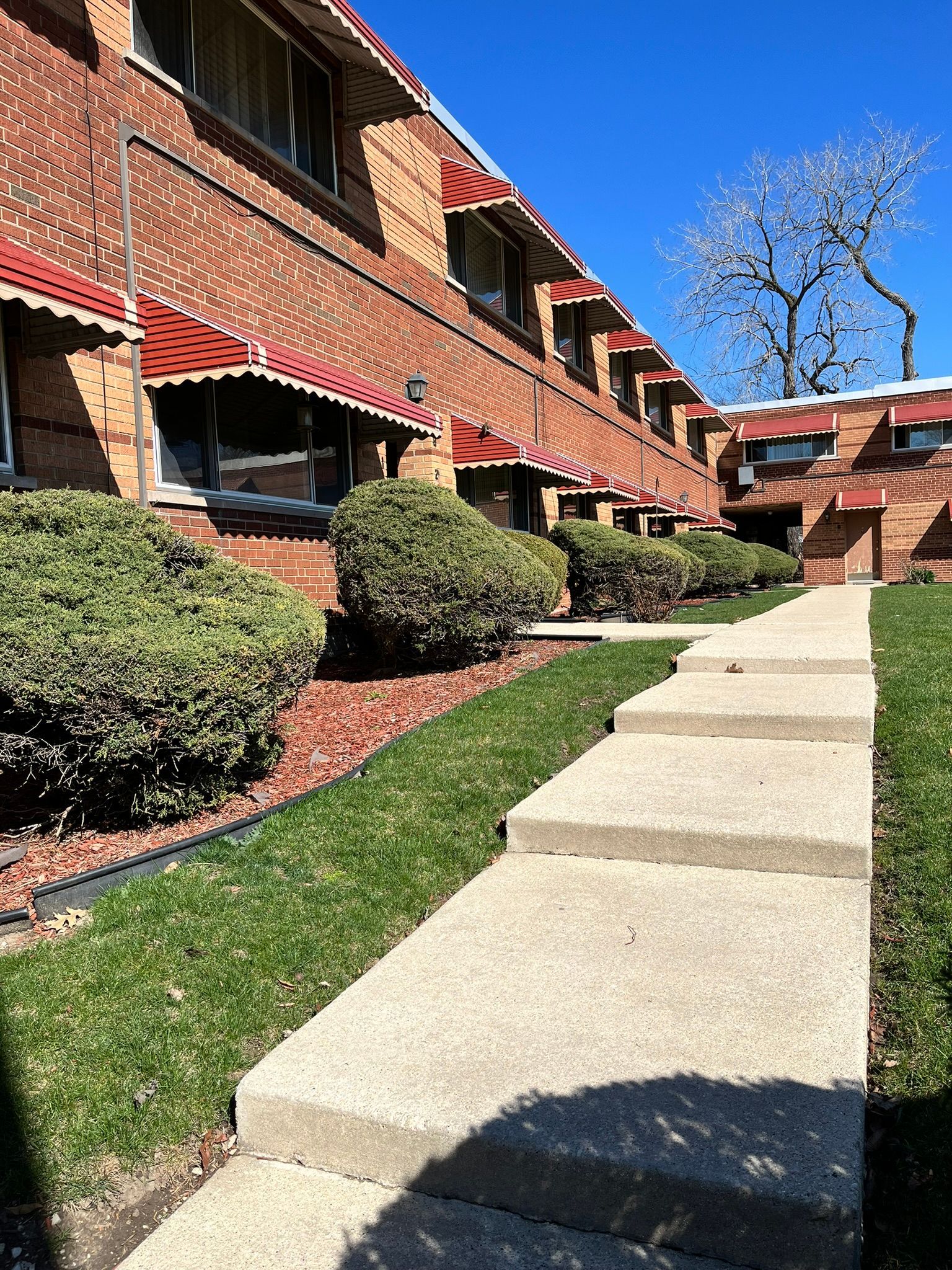 a sidewalk leading to a brick building with red awnings .