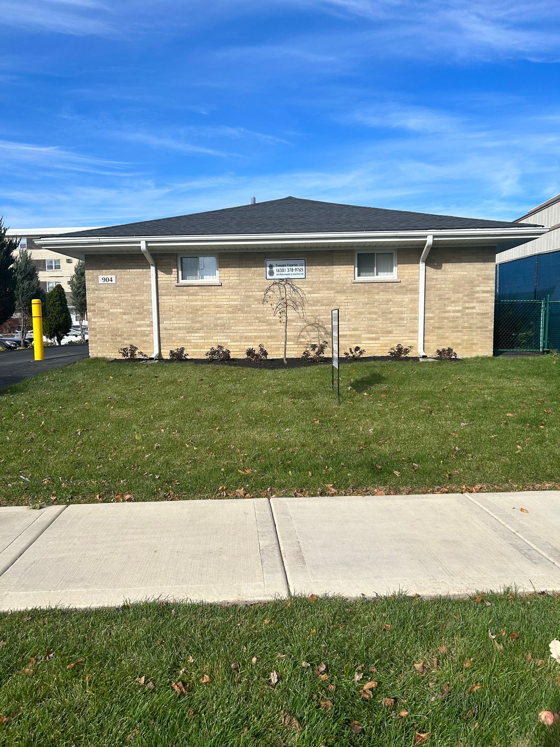 a brick house is sitting on top of a lush green lawn next to a sidewalk .