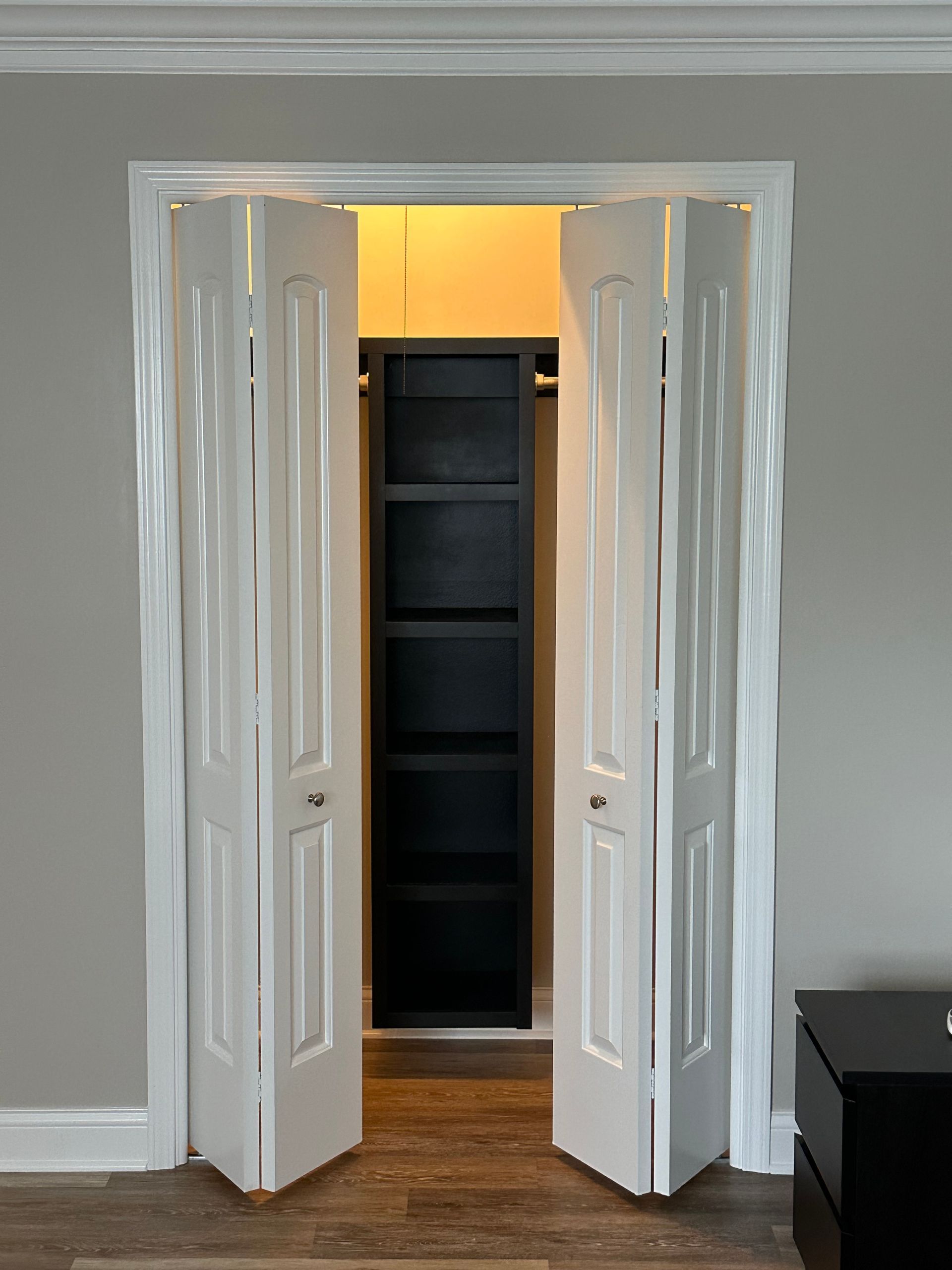 a closet with the doors open and a black shelf inside .