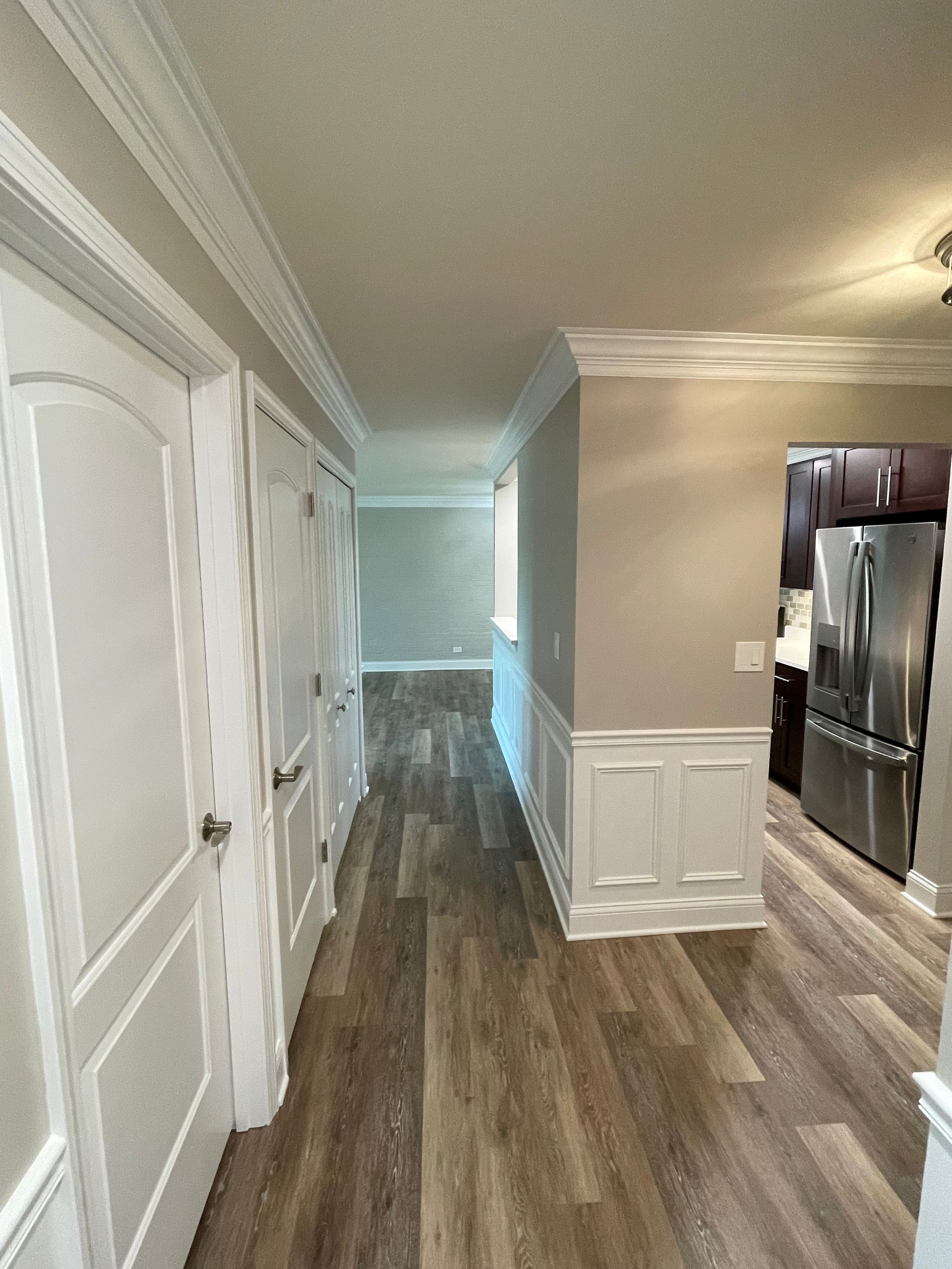 a long hallway leading to a kitchen with hardwood floors and stainless steel appliances .