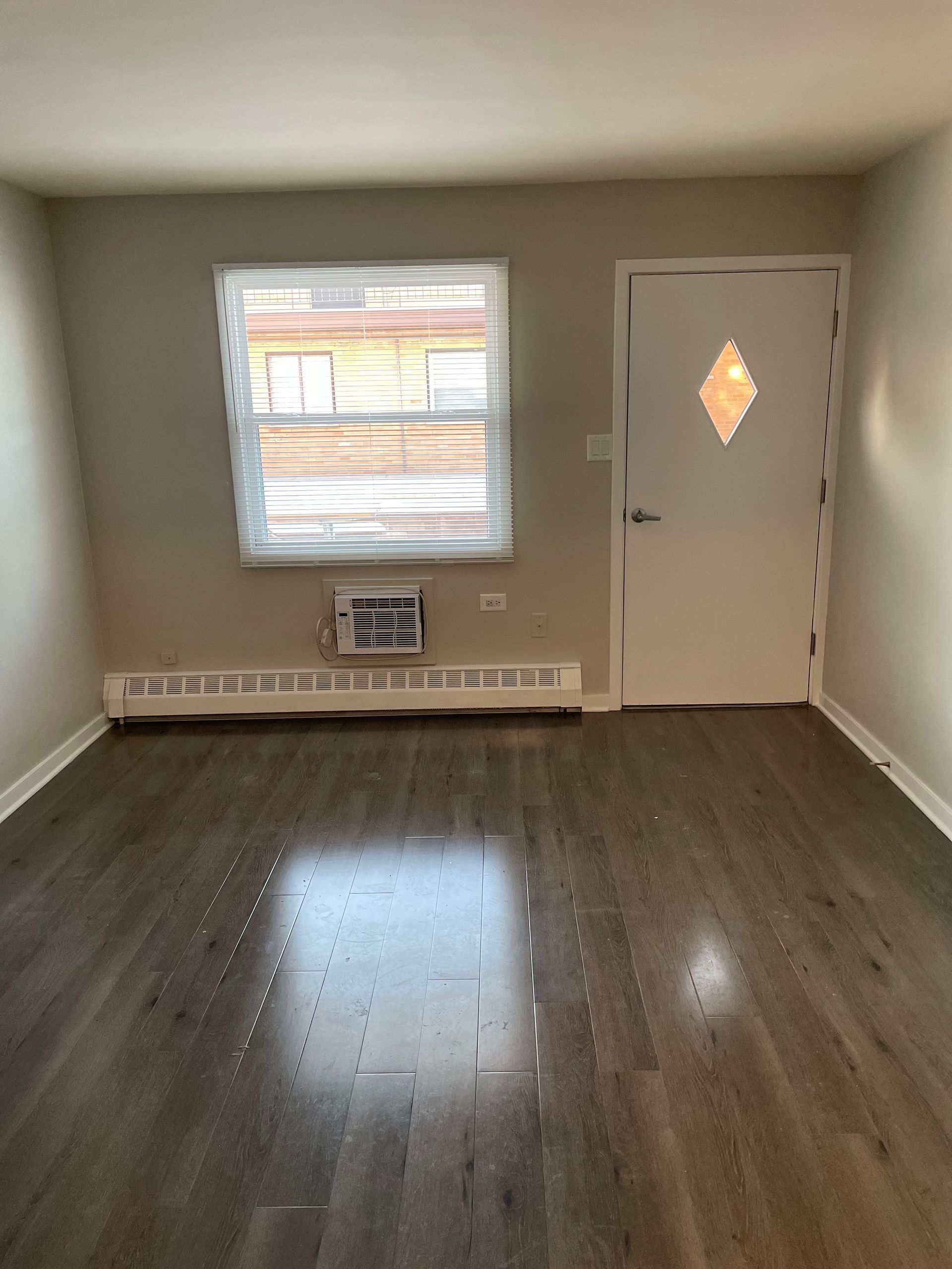 an empty living room with hardwood floors and a window .