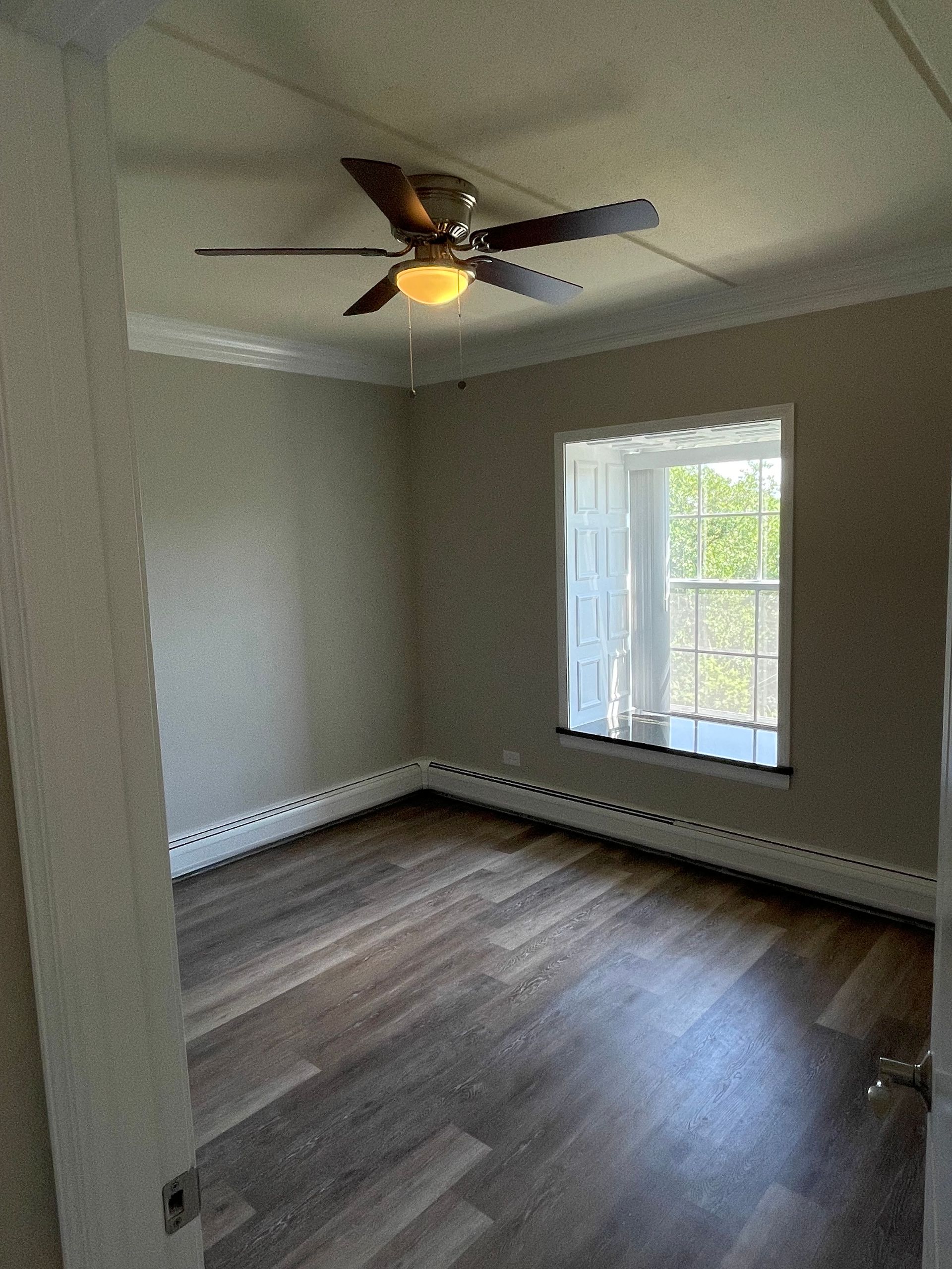 An empty room with a ceiling fan and a window.