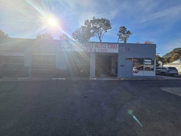 Man in jacket on phone, examining tires in a store. Man on phone examines tires in a store, wearing a brown jacket.