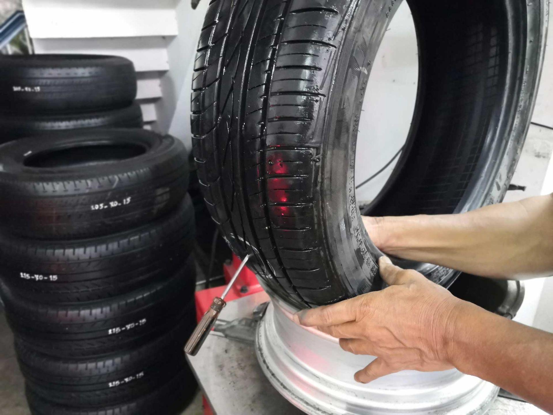 Person removing a tire from a rim with a tool; stack of tires in the background.