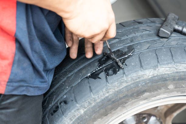 Person fixing a car tire, inserting a tire plug into the damage with a tool.