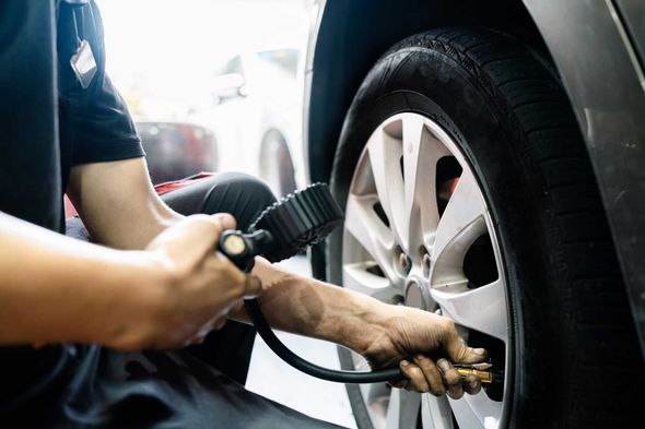 Mechanic inflating a car tire with a pressure gauge.