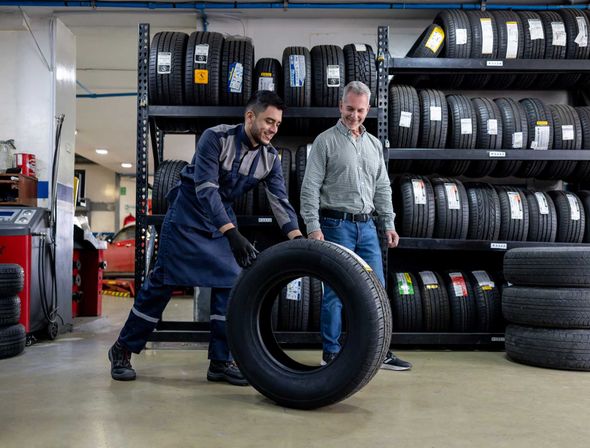 Mechanic rolling a tire towards a customer in a tire shop.