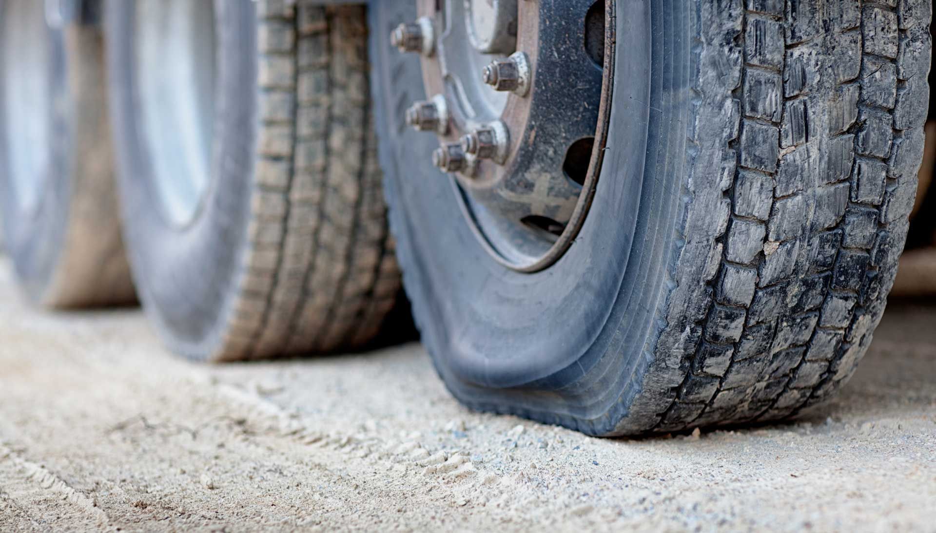A truck's flat tire on a sandy surface. Close-up of deflated rubber against the rim.