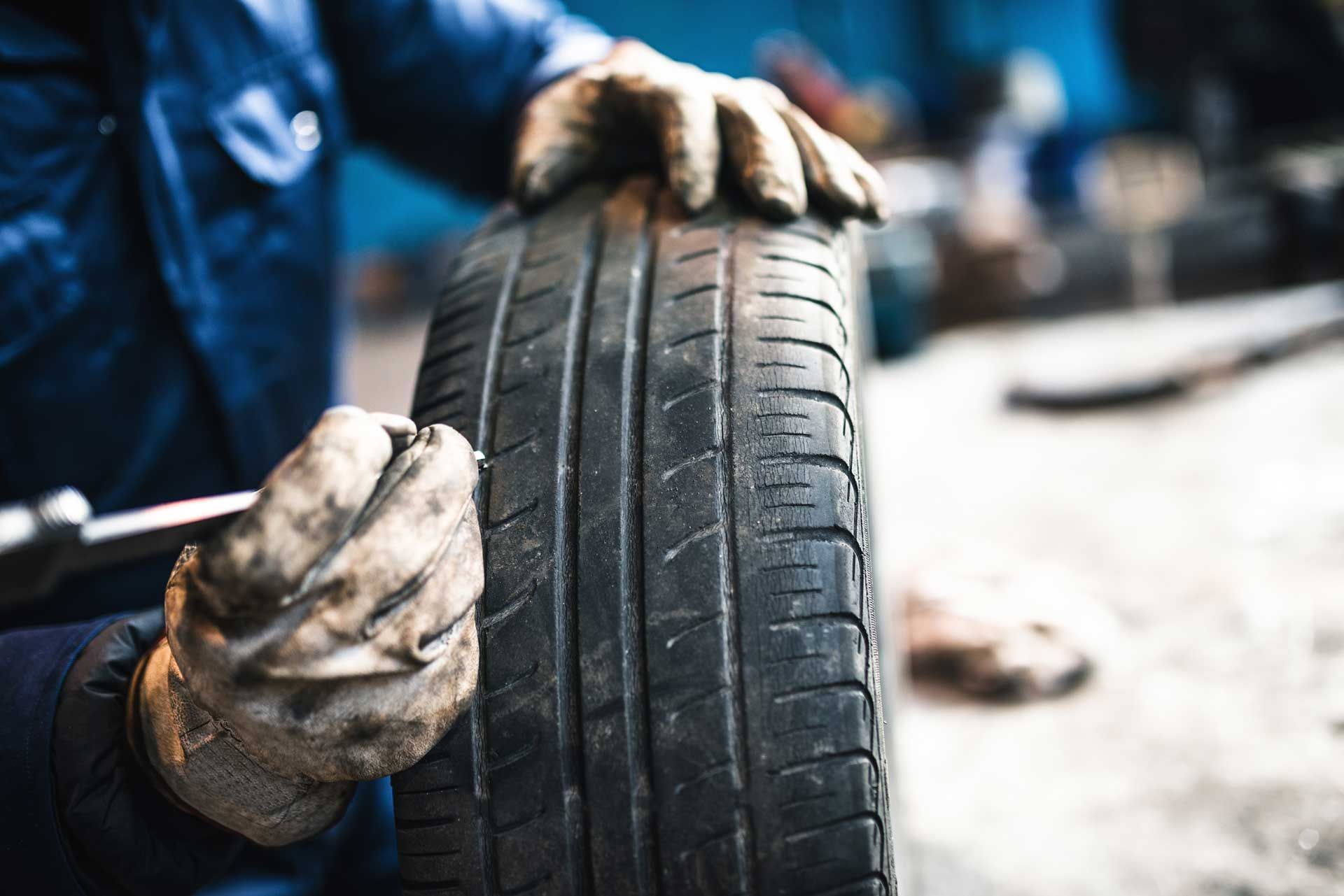 Mechanic in blue coveralls and gloves inspecting a tire in a garage.