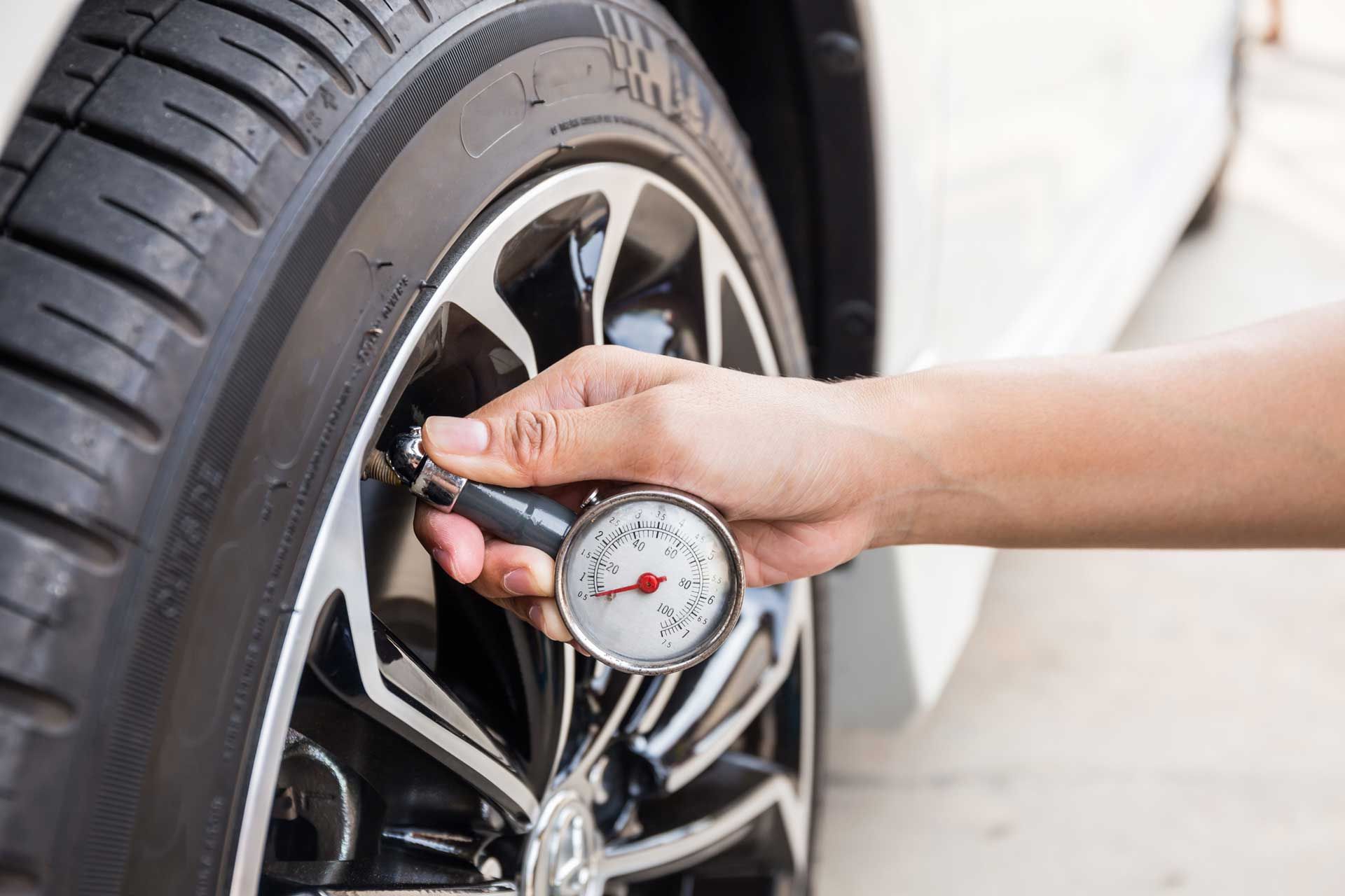Person checking tire pressure with a gauge on a car tire.