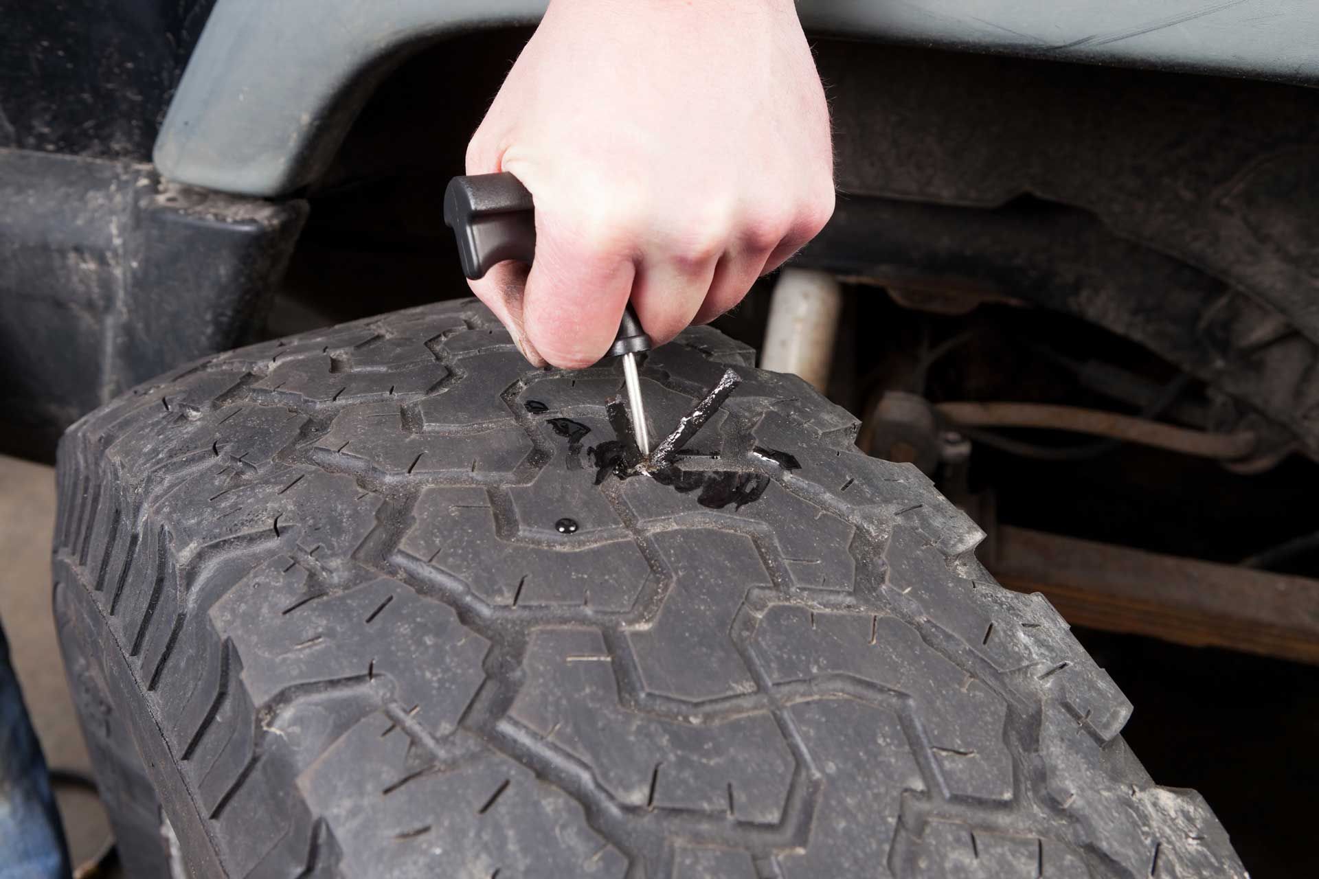 Person using a tool to repair a flat tire on a vehicle, outdoors.