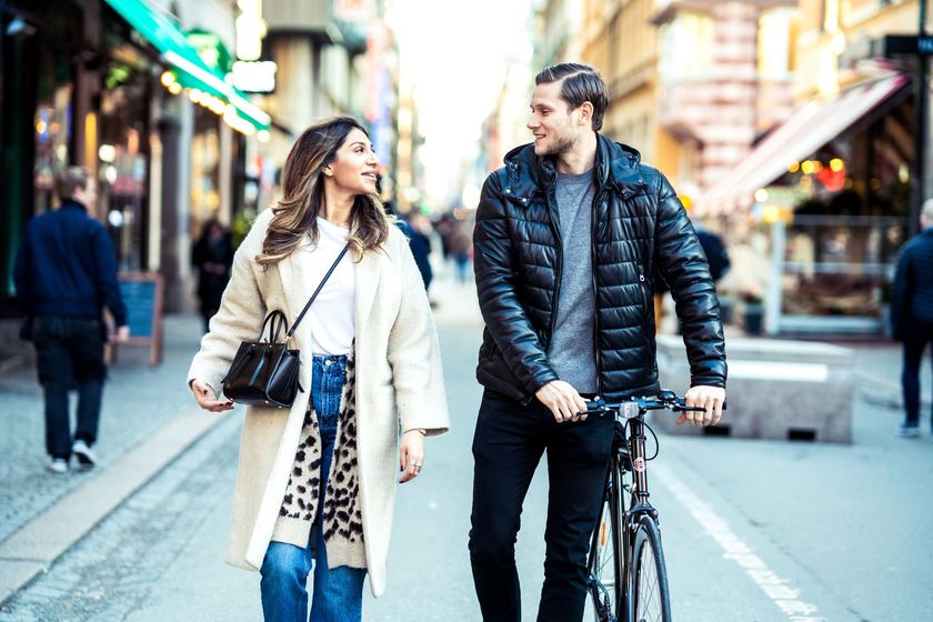 a man and a woman are walking down a city street with a bicycle .
