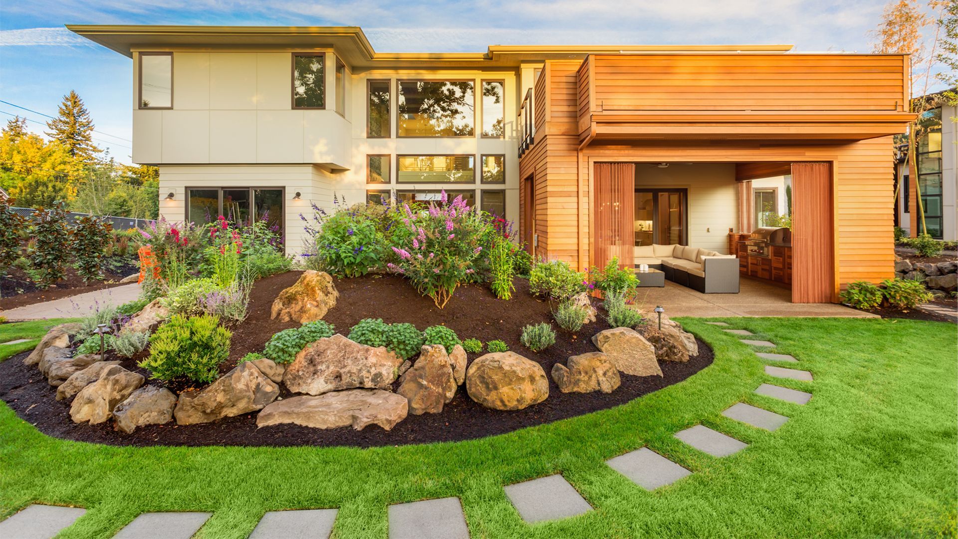 A large house with a lush green lawn and a rock garden in front of it.