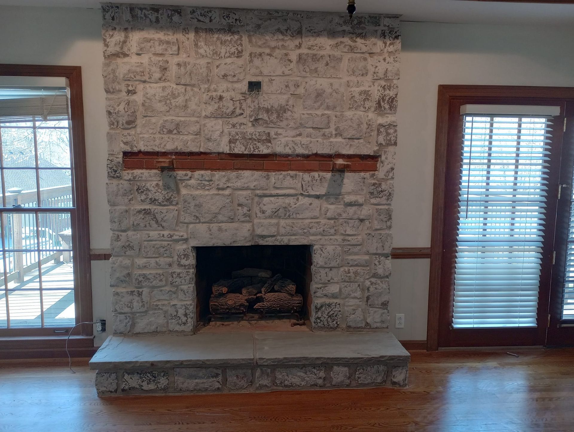 Stone fireplace with wooden mantel and hearth between windows, with a view.