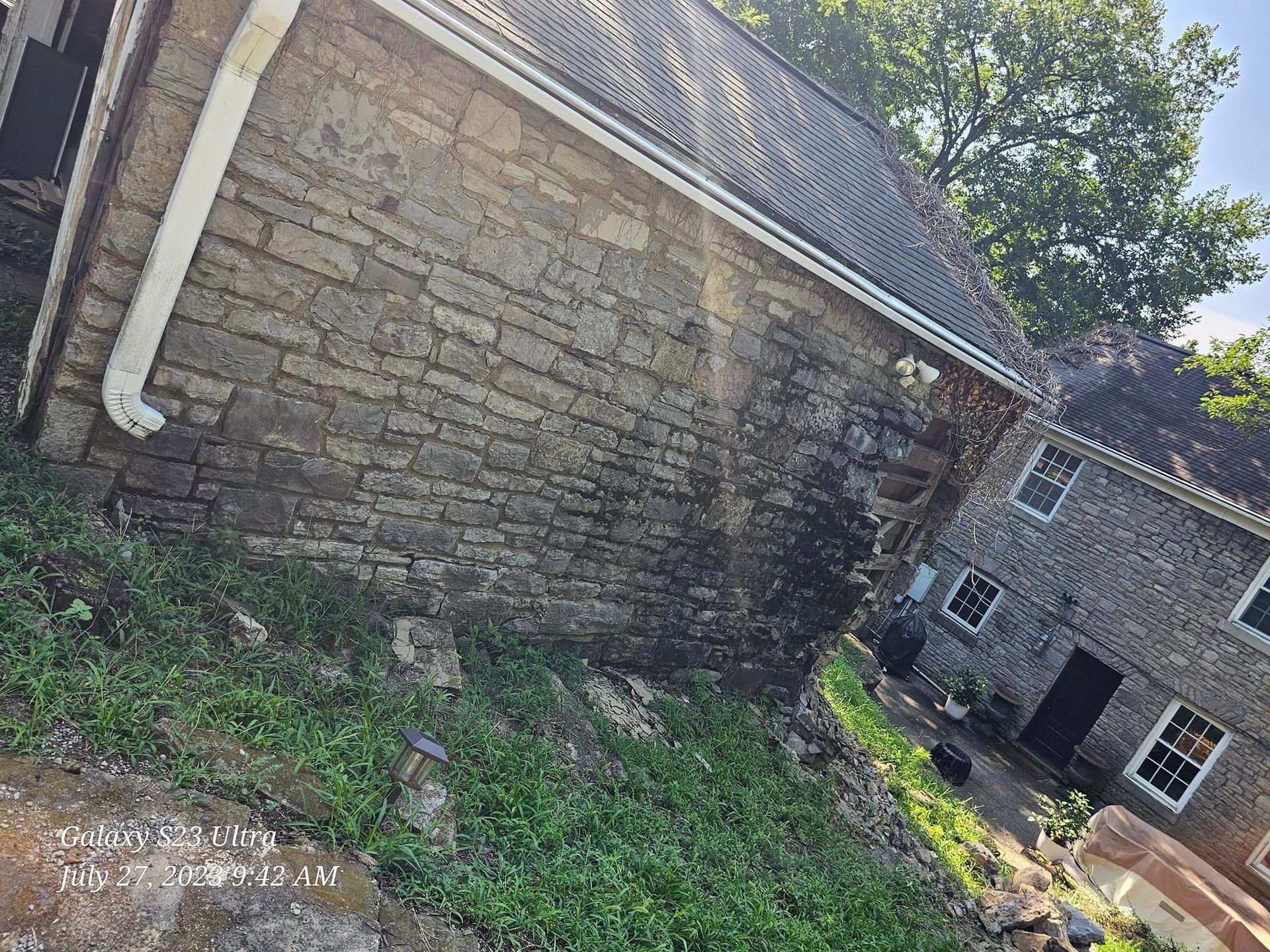 Stone building with a dark roof, white gutters, and a grassy hill in front.