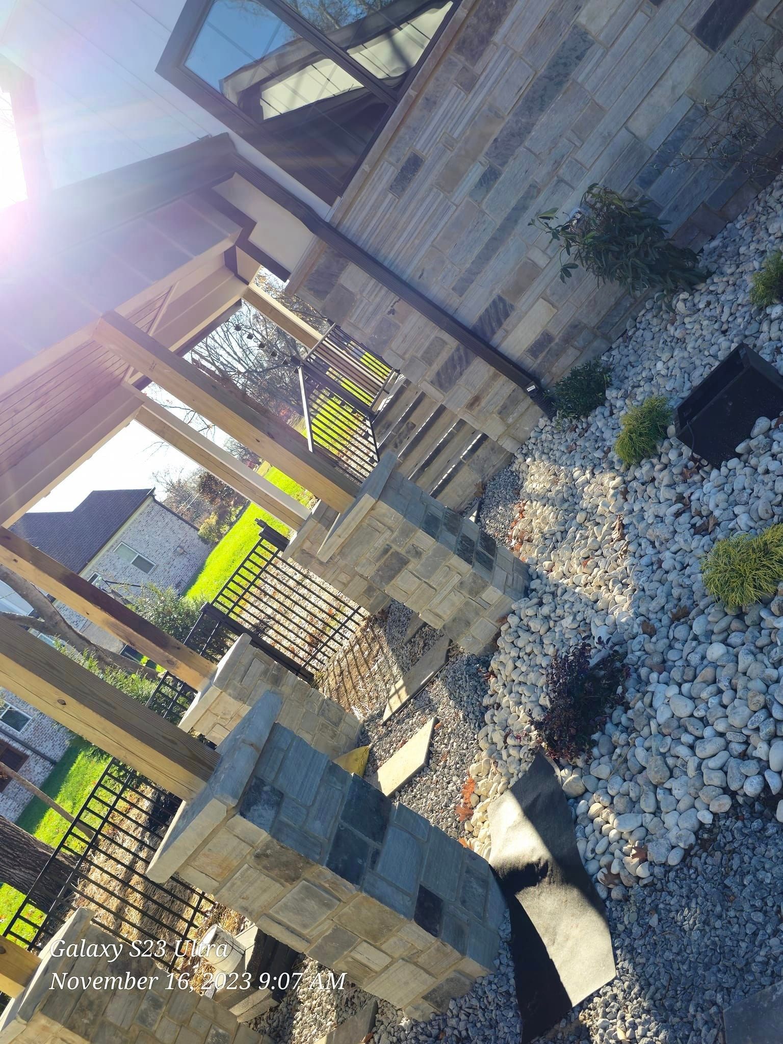 Stone patio with gravel, plants, wooden trellis, and building facade.