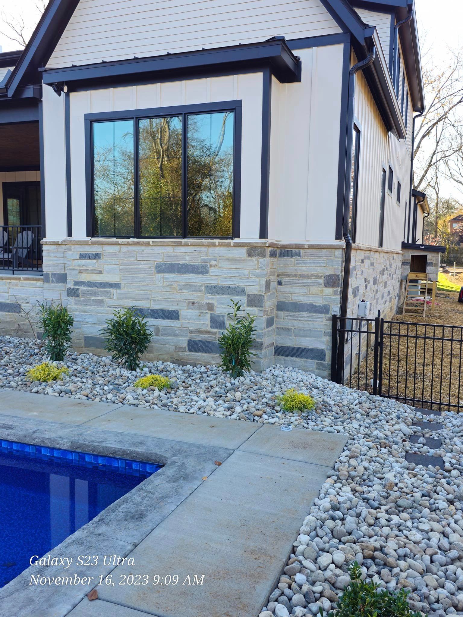 Exterior of a house with stone accents, a pool, landscaping, and a black fence.