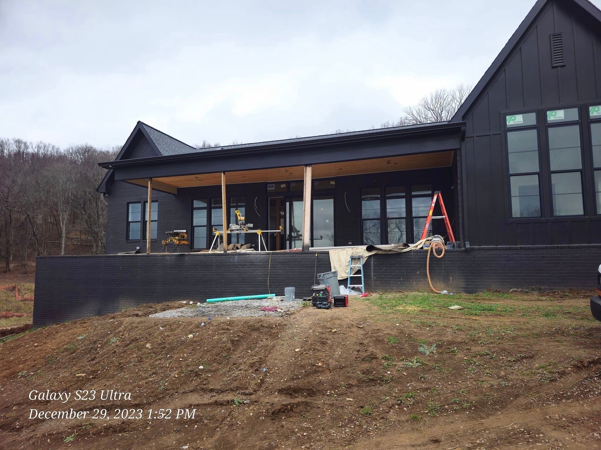 Black house under construction; porch with exposed wood, window installation, outdoor setting.