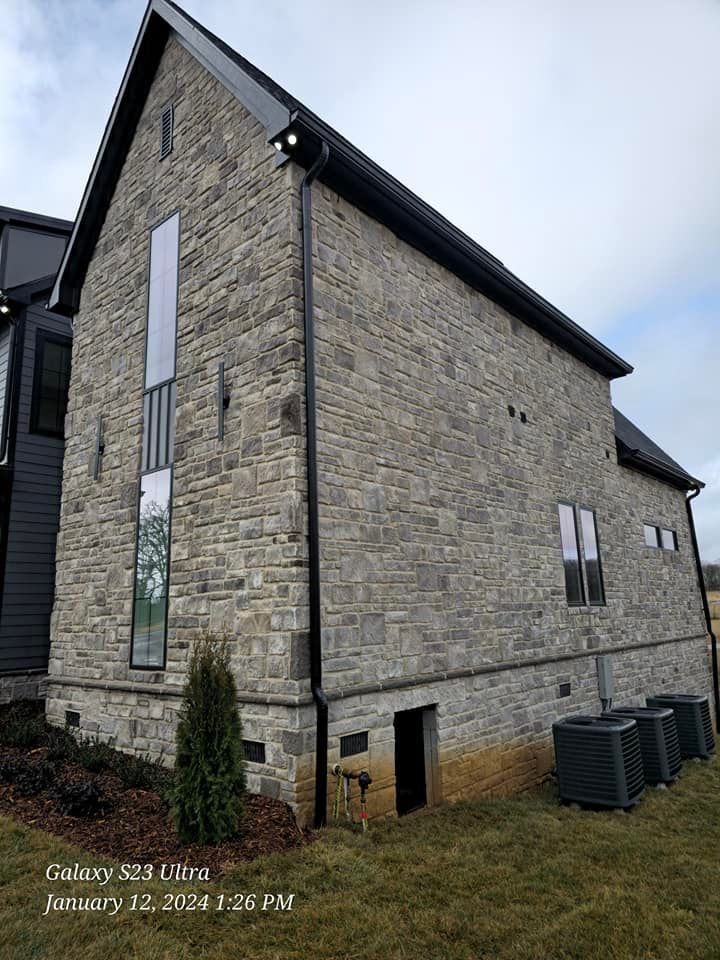 Stone-clad modern house with a tall window, black trim, and air conditioning units outside.
