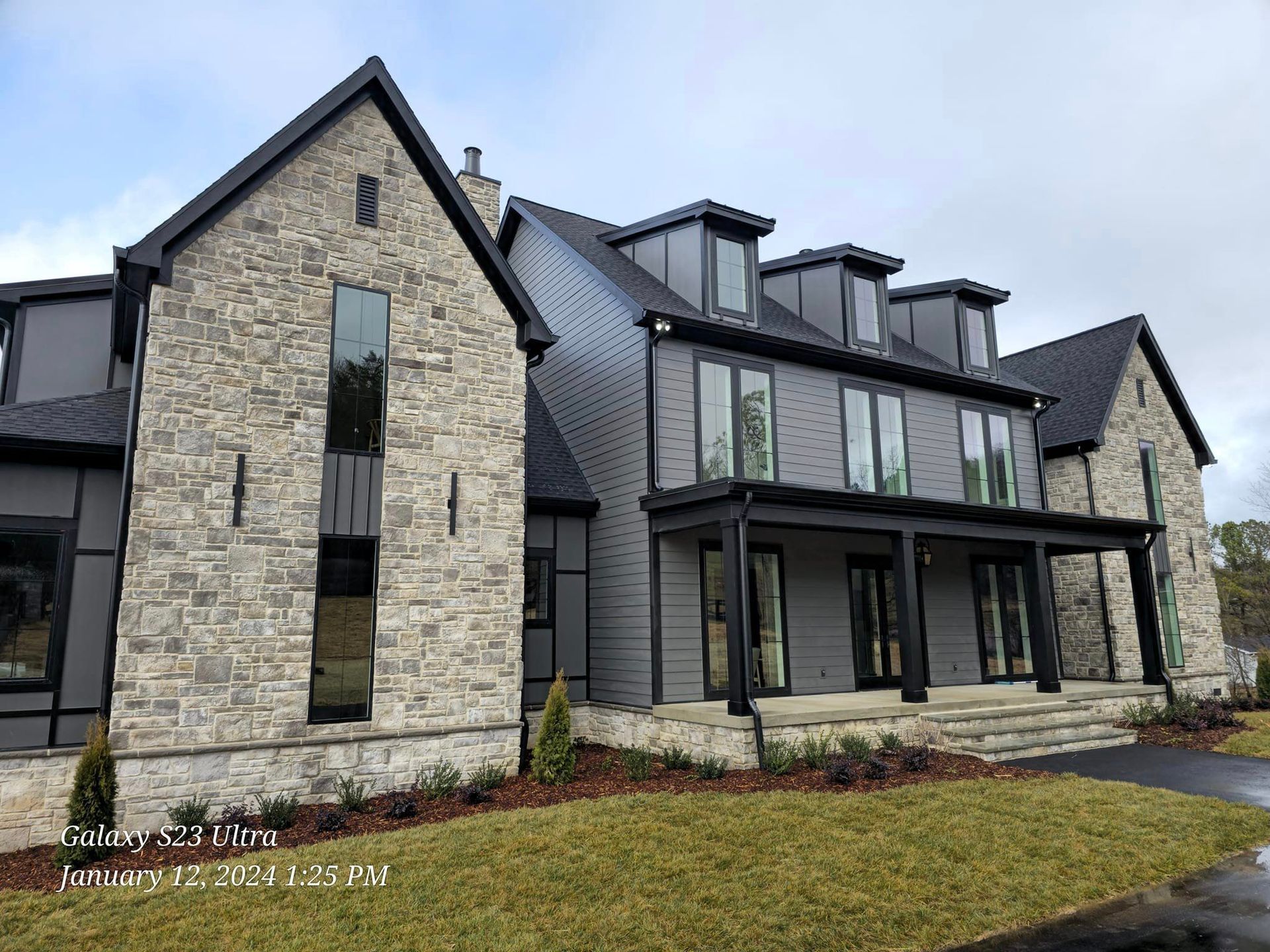 Modern gray and stone house with black trim and multiple windows.