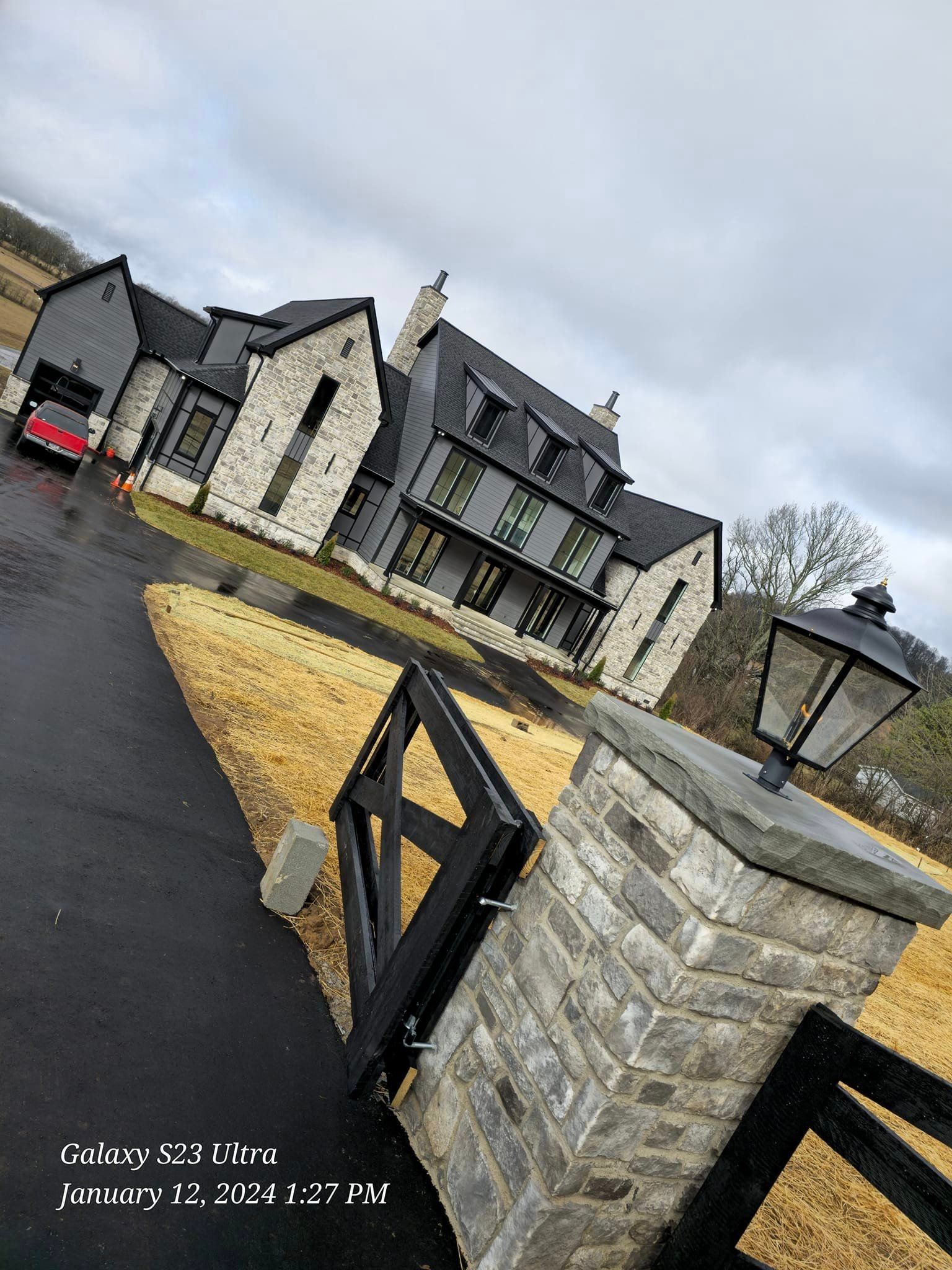 A modern home with stone and black accents, a gated entrance, and a long driveway.