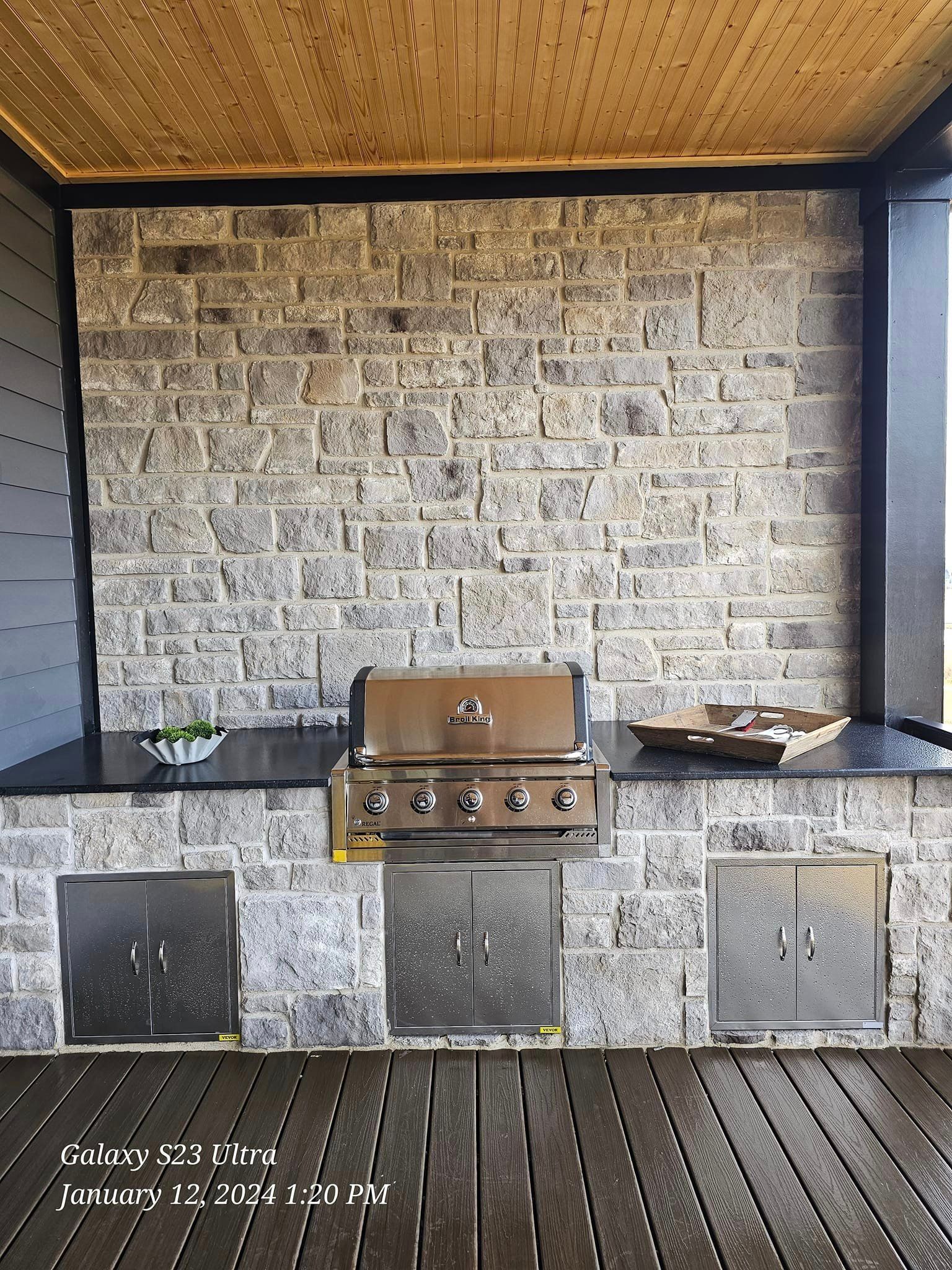 Outdoor grilling station with stainless steel grill, brick wall, and wooden deck.