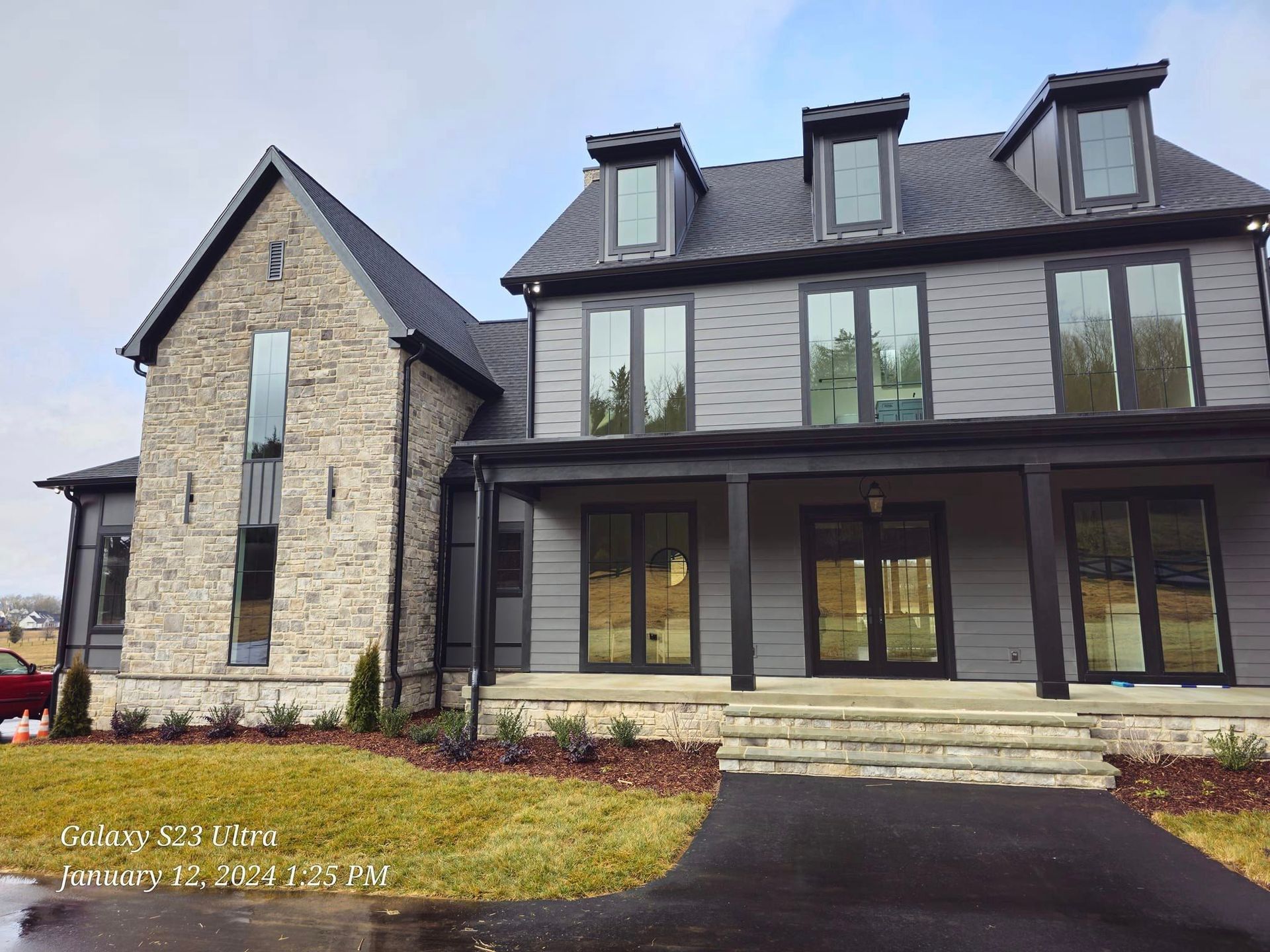 Gray and stone facade house with black trim, windows, and a covered porch.