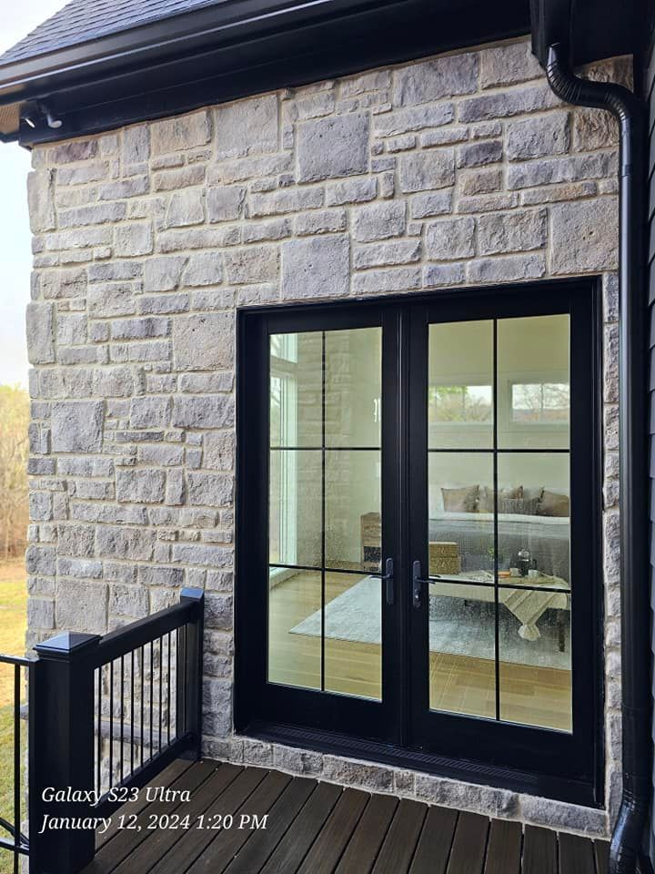 Stone exterior wall with black framed glass doors and a black railing.