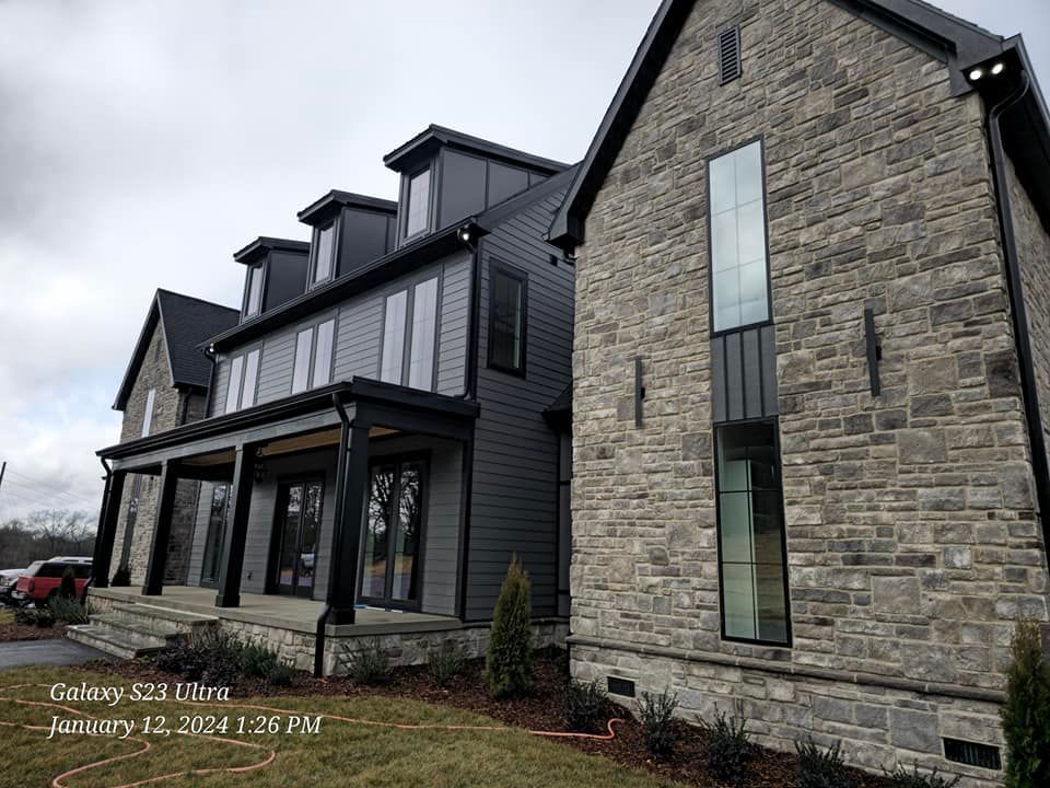A modern two-story house with dark gray siding and stone facade on a cloudy day.