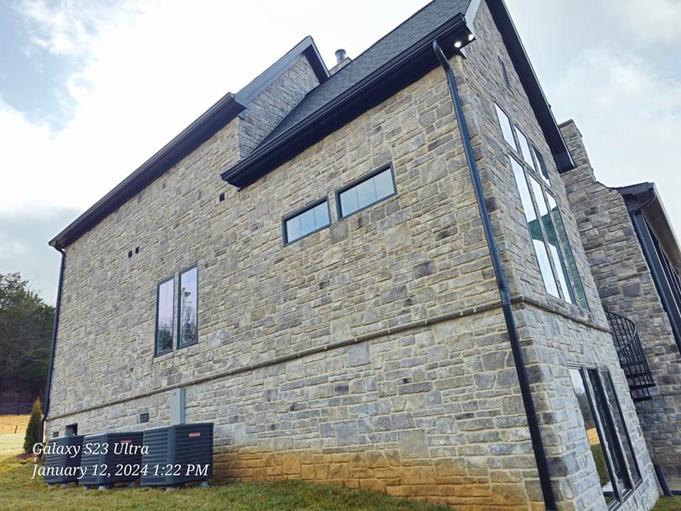 Stone-faced house exterior with black trim and multiple windows under a cloudy sky.