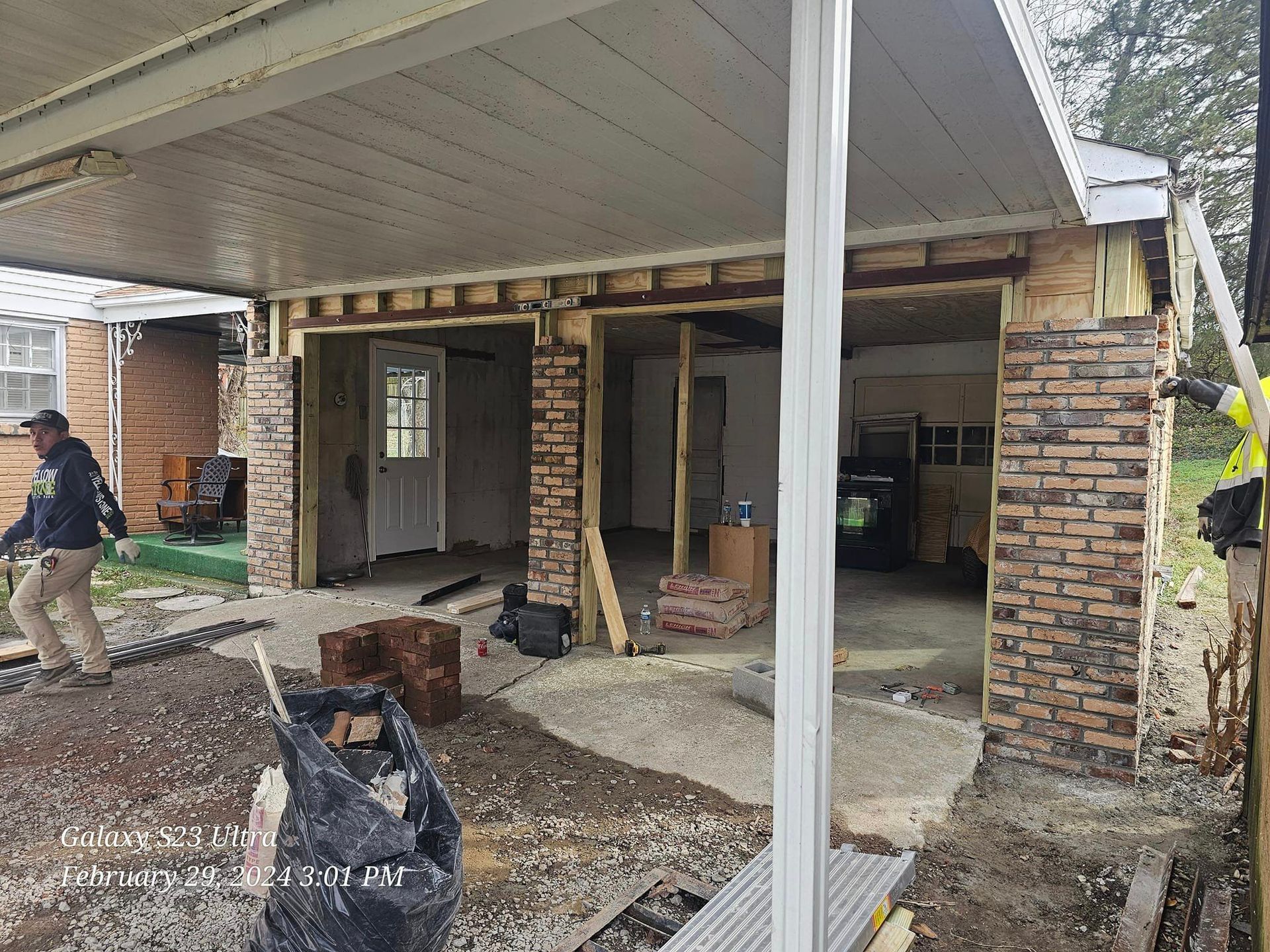 Construction site: garage renovation with exposed framing, brick columns, and worker.
