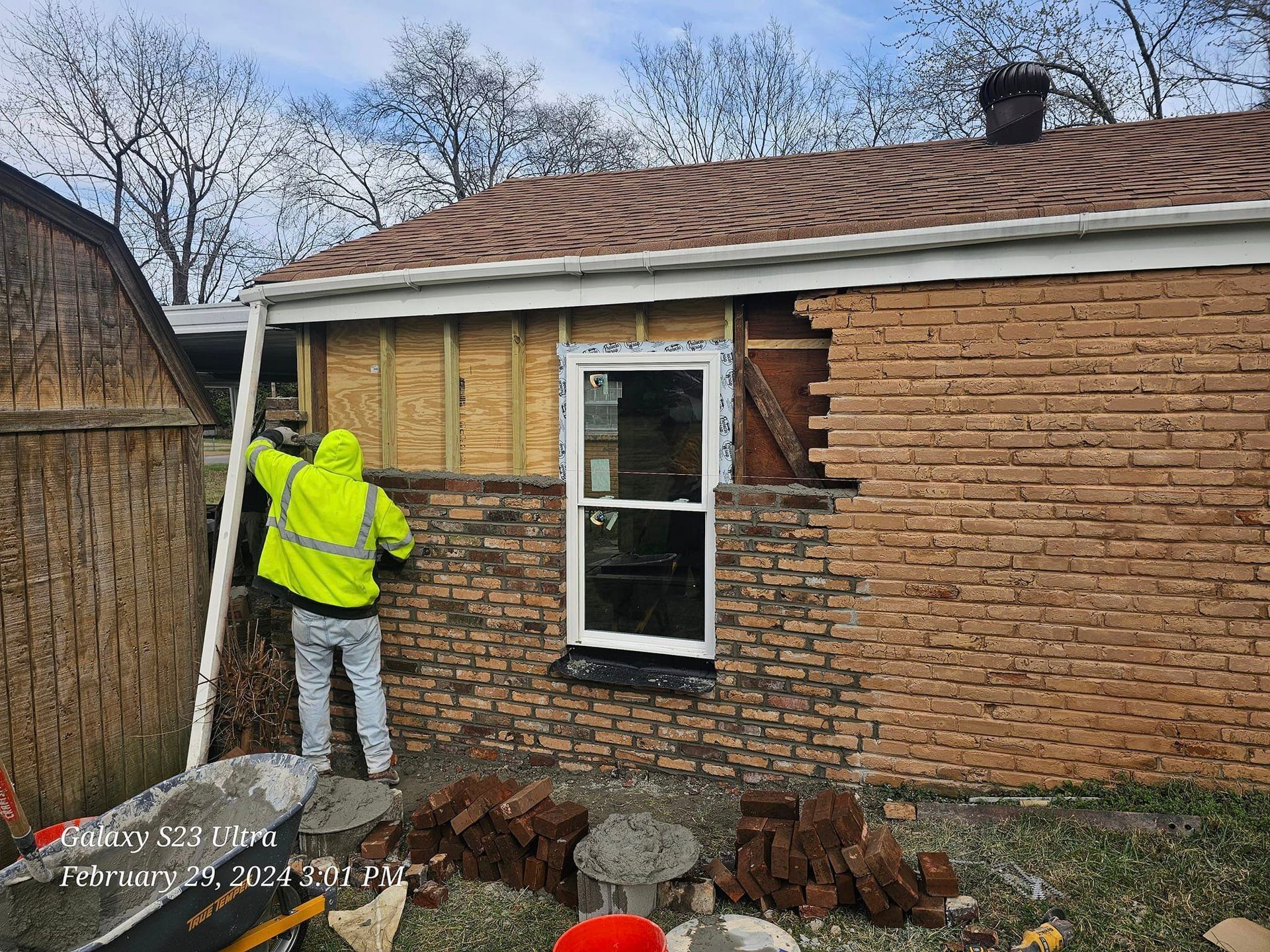 Man in neon jacket laying brick on a building, window installed.