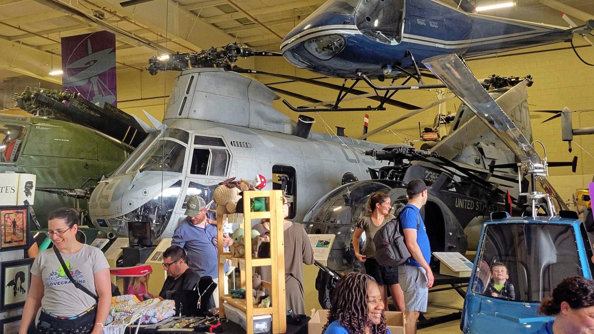Helicopters on display, inside a museum with people browsing.