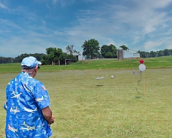 Man in blue shirt watches a small plane flying over a grassy field with targets.