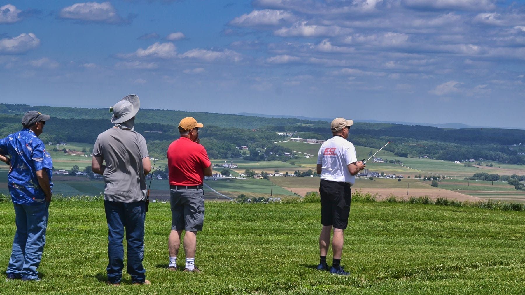 Four people looking out over a green valley, under a blue sky with clouds.