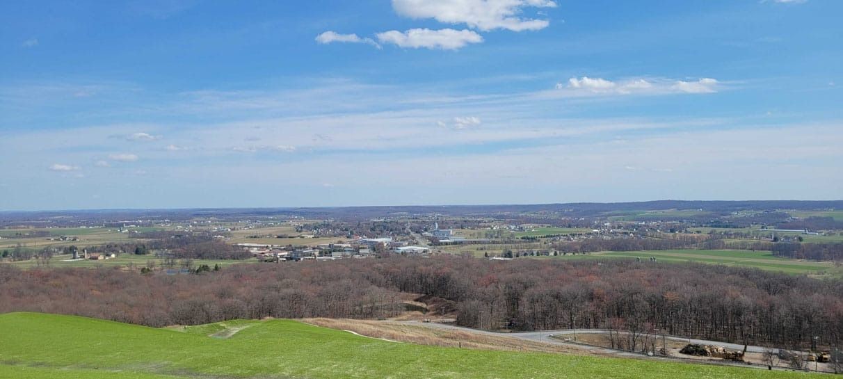 Rolling green hills and a town under a blue sky with white clouds.