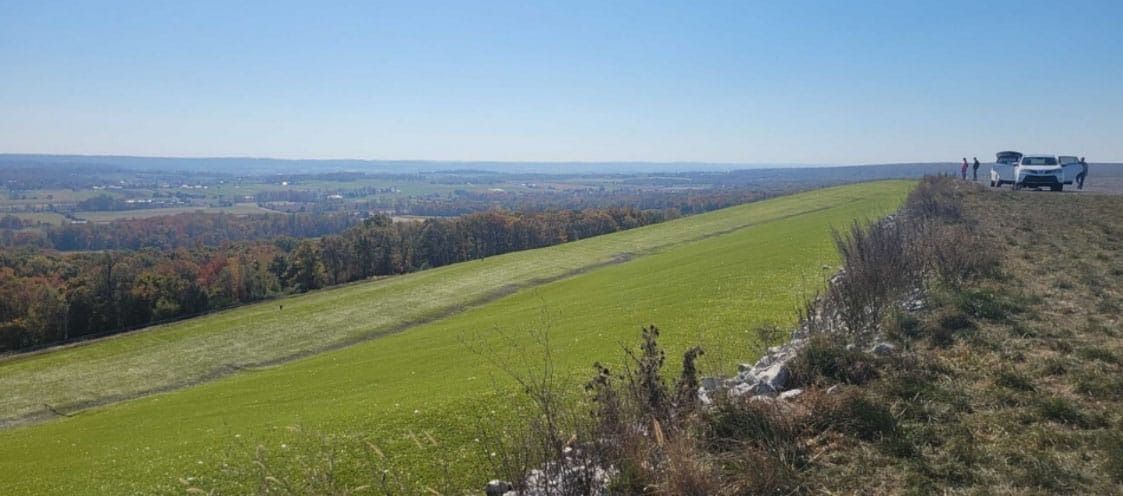 A long green dam with a vehicle parked on the edge, clear blue sky overhead.