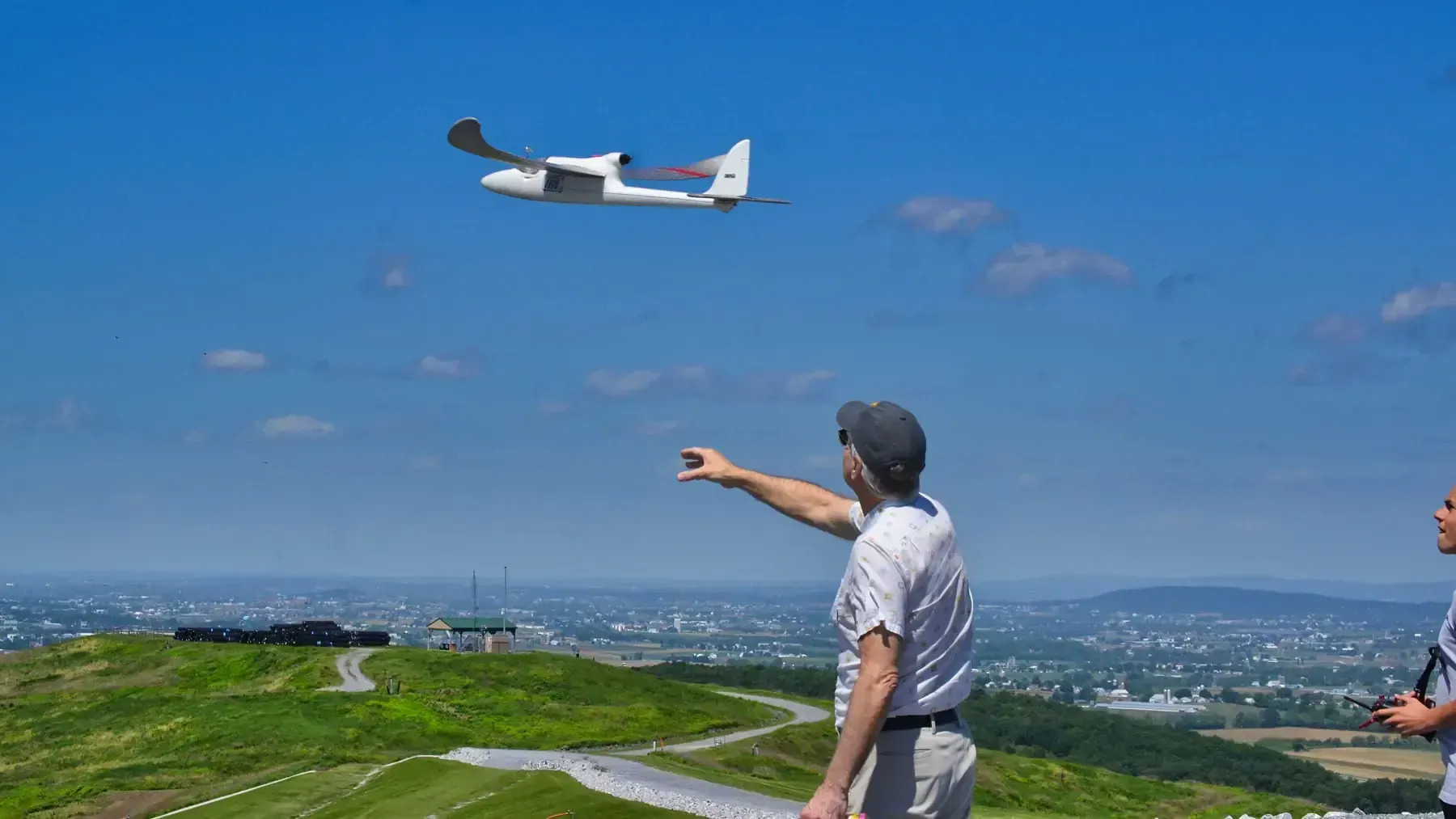 Man launching a drone, pointing towards the sky, with city in the background. Sunny day.