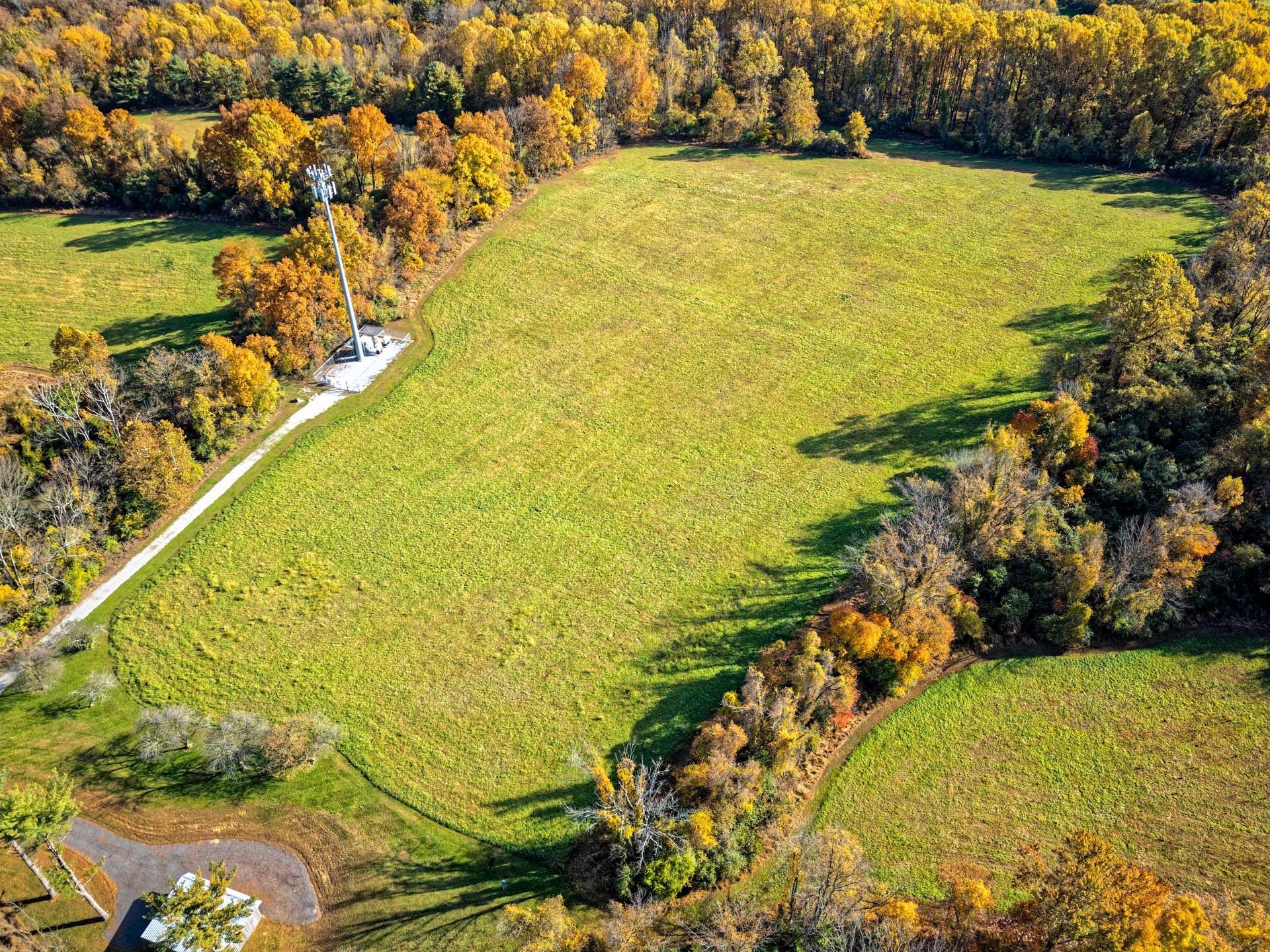 Aerial view of a field surrounded by trees in autumn, with a communication tower.