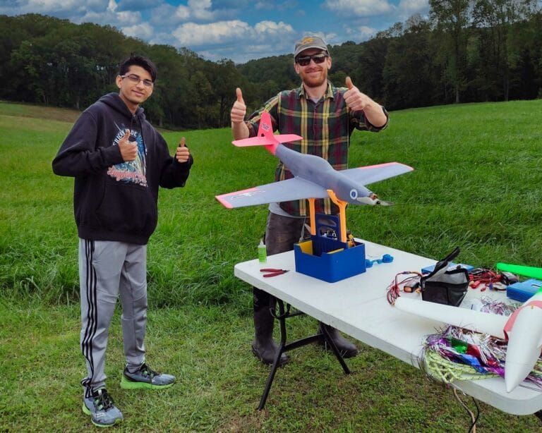 Aerial view of a rectangular field, light green, surrounded by vibrant green grass and trees.
