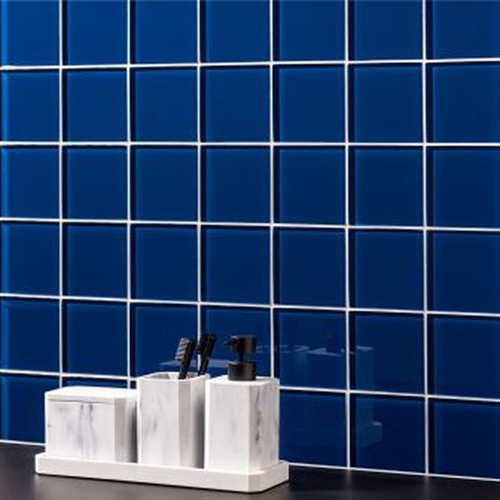 Blue tiled wall with white grout. Marble bathroom accessories: soap dispenser, toothbrush holder, and storage container.