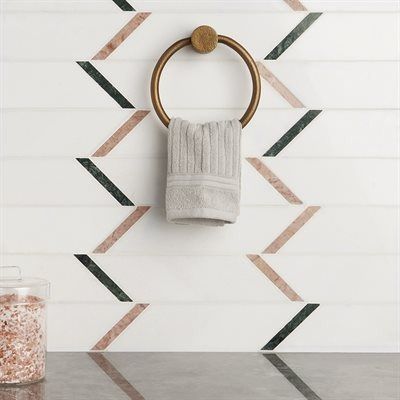White tile wall with chevron pattern of pink and green, a brass towel ring, and gray towel.