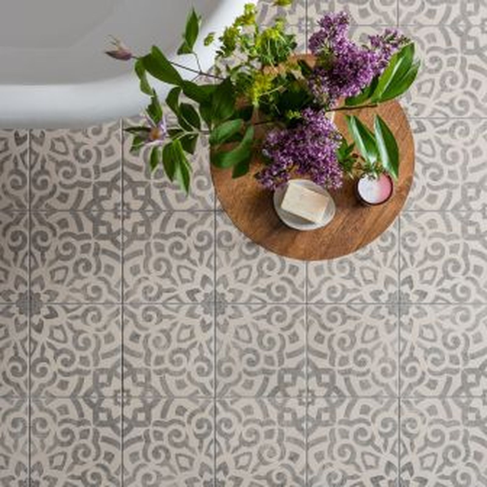 Floral tile bathroom floor with wooden tray holding flowers, soap, and cosmetics next to a tub.