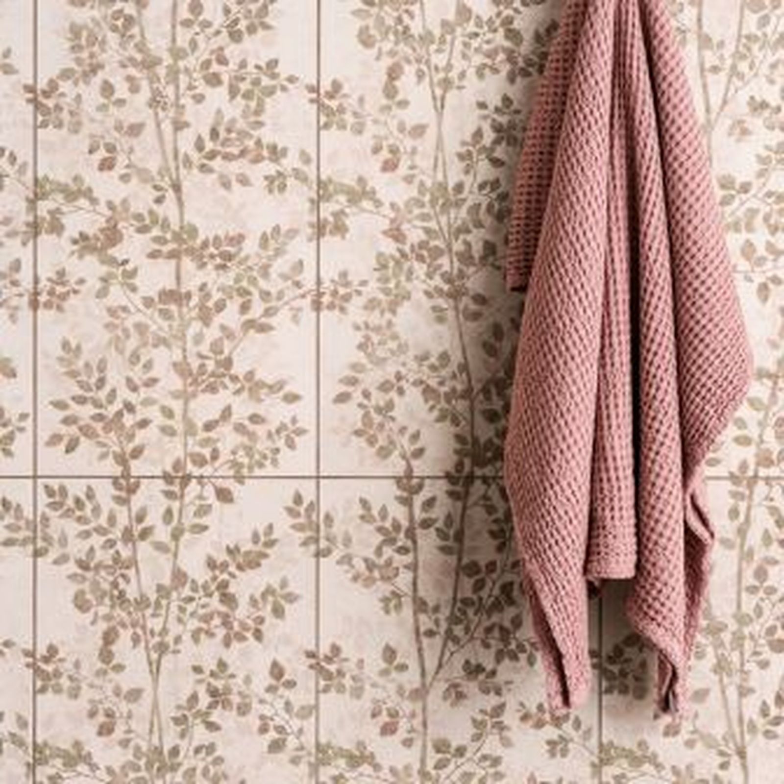 Pink towel hanging on a wall with a tree-leaf pattern.