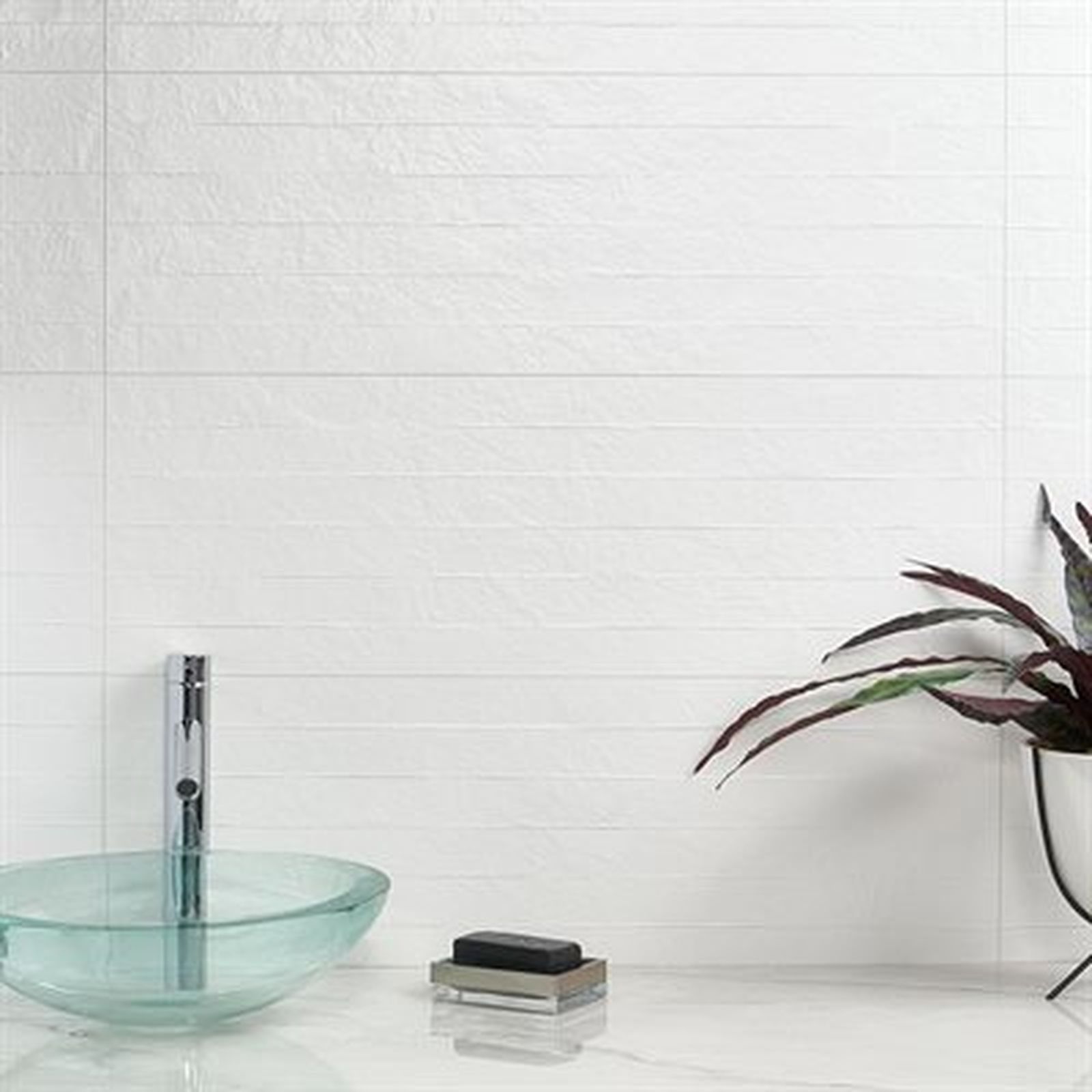 Modern white bathroom with glass sink, soap, and plant.