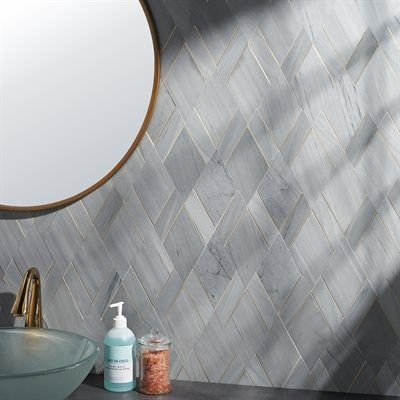 Bathroom wall with gray diamond-patterned tile, gold accents, round mirror, and gold faucet.