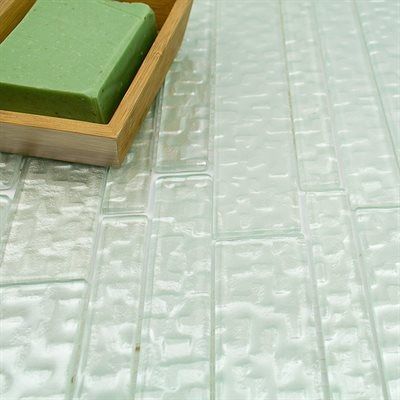 Green soap in a wooden soap dish on a light-colored, textured, rectangular tile surface.
