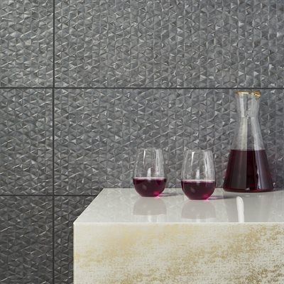 Gray textured tile wall with white countertop holding two glasses and a carafe of red liquid.