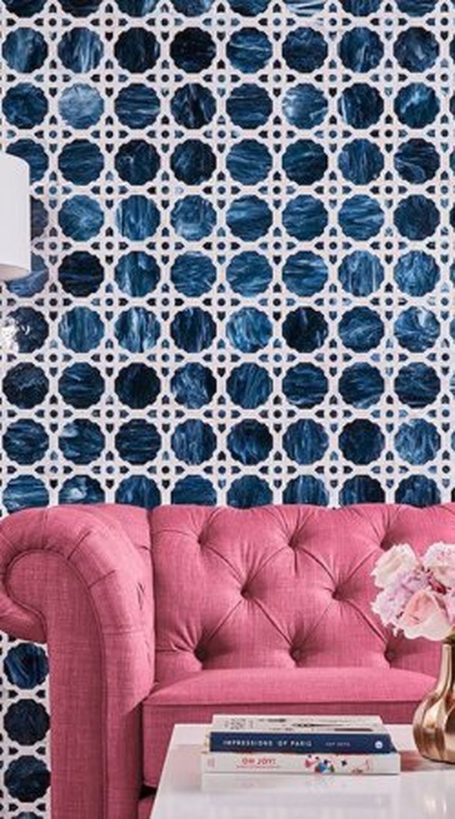 Pink tufted sofa against a blue and white patterned wall; white table with books and flowers.